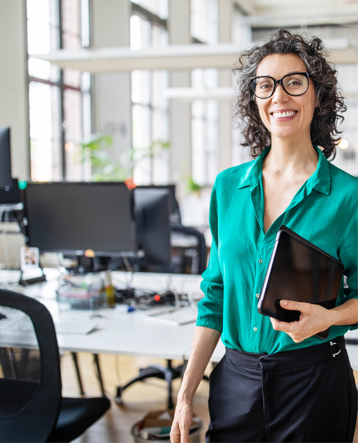Portrait of mature businesswoman in casuals standing at her desk with digital tablet  Woman entrepreneur in office looking at camera and smiling 